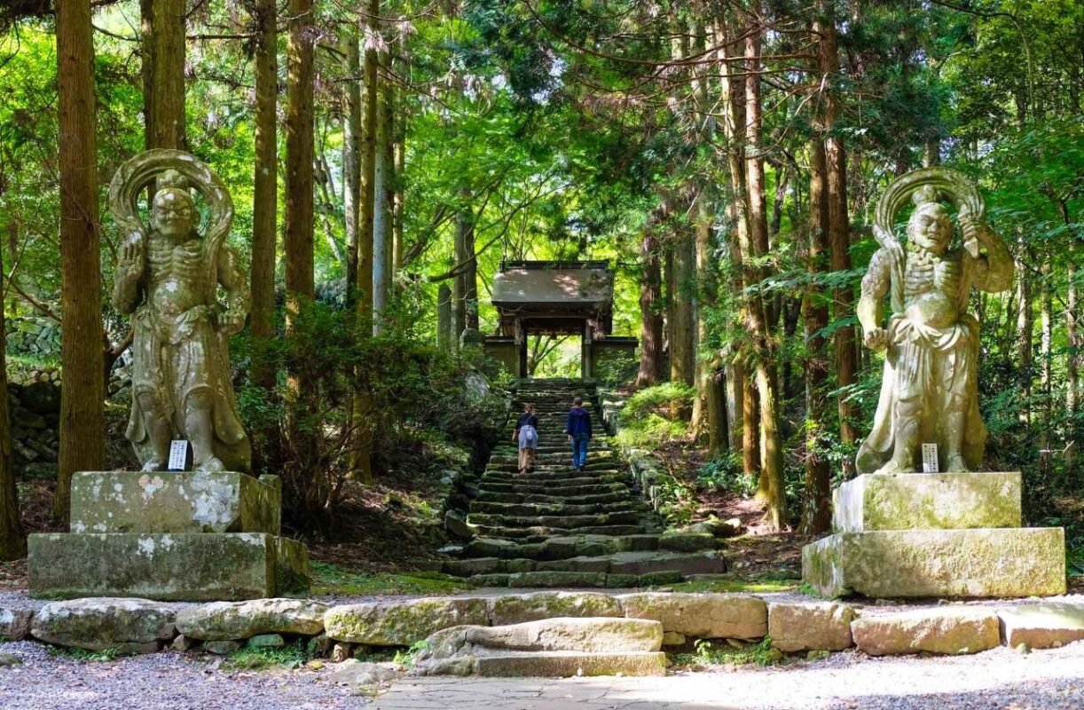 Escalier de pierre moussu entre deux statues de gardiens Niō, menant à un temple dans une forêt de cèdres au Japon